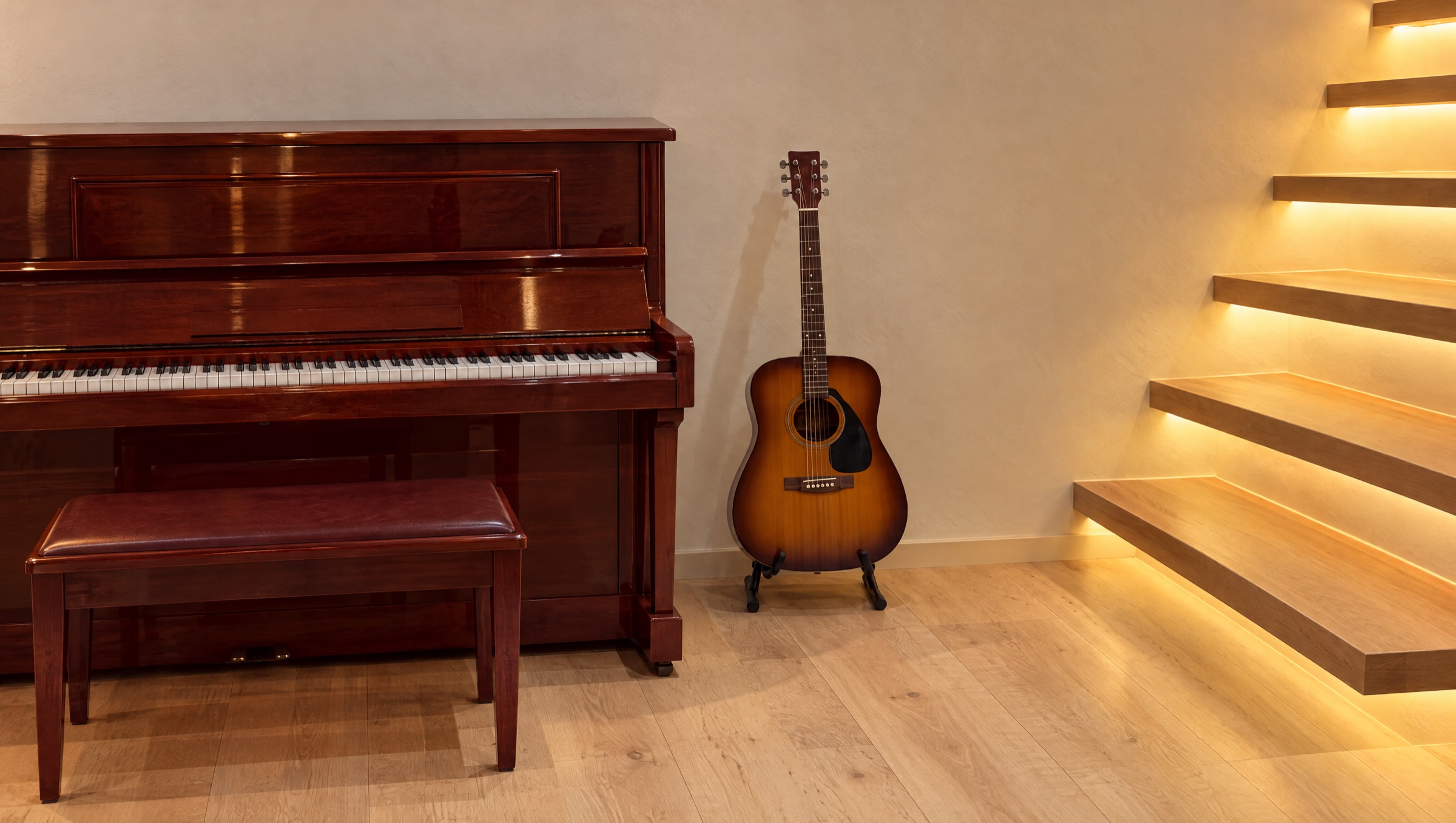A mahogany piano and an acoustic guitar beside softly lit floating stairs